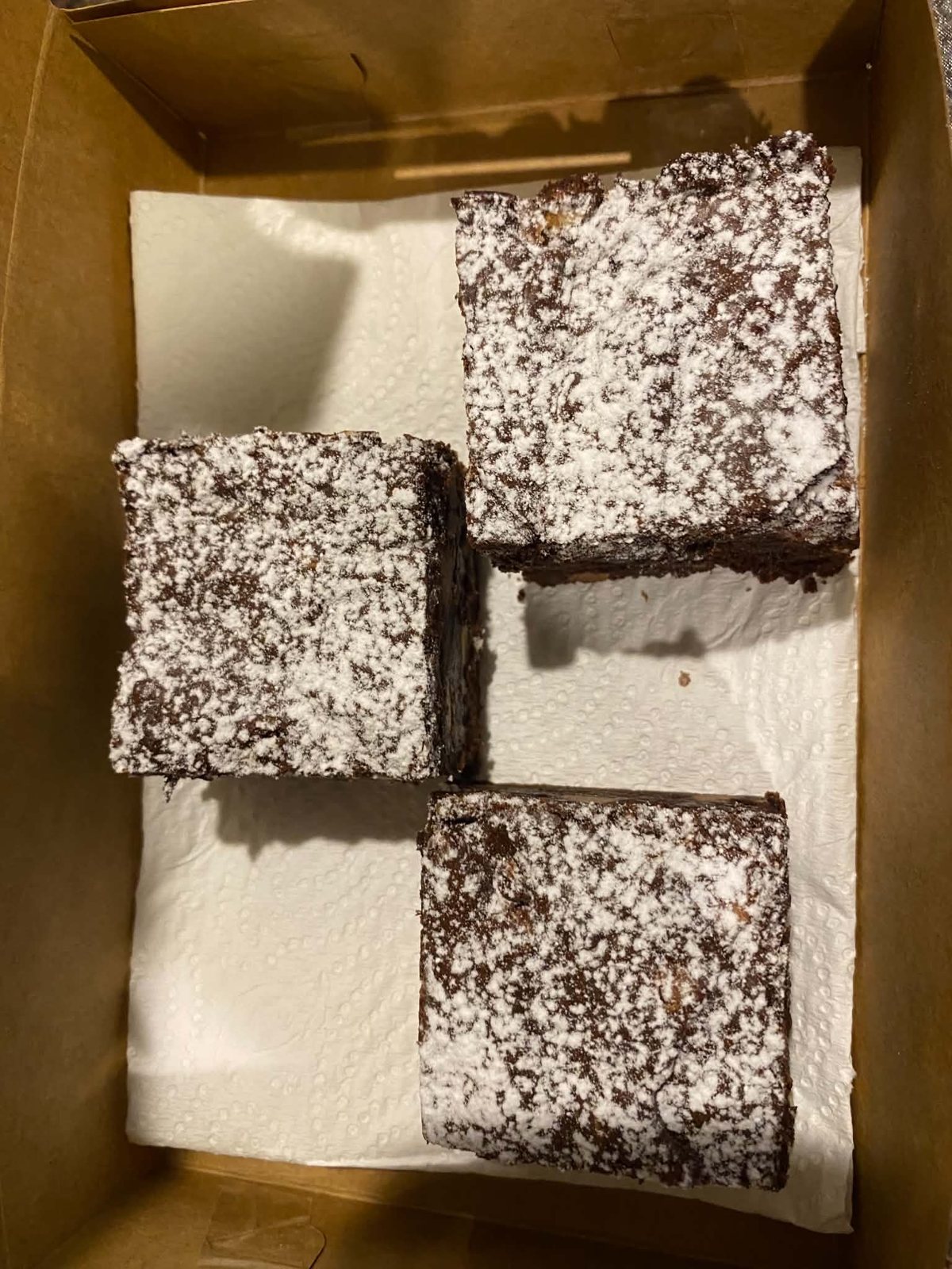 Three icing-sugar-dusted brownies in a parchment-lined kraft box.